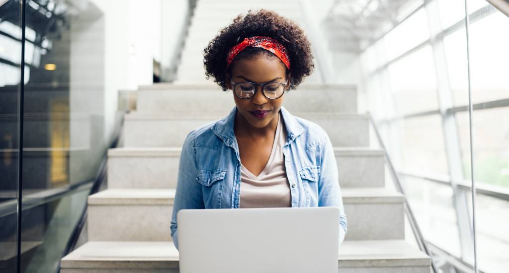 Focused young African student sitting on stairs using a laptop Focused young African student sitting on stairs using a laptop