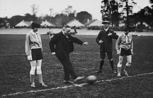 As meninas do Dick, Kerr's Ladies tinham uma agenda lotada, jogando mais de 60 partidas em um ano. Apesar disso, elas conseguiam conciliar o trabalho na fábrica. Nesta fotografia, o time estava representando a Inglaterra em um jogo contra a França, em Herne Hill, em 1925. Nela, o músico George Robey (1869 - 1954) faz um chute contra o gol. As meninas do Dick, Kerr's Ladies tinham uma agenda lotada, jogando mais de 60 partidas em um ano. Apesar disso, elas conseguiam conciliar o trabalho na fábrica. Nesta fotografia, o time estava representando a Inglaterra em um jogo contra a França, em Herne Hill, em 1925. Nela, o músico George Robey (1869 - 1954) faz um chute contra o gol.
