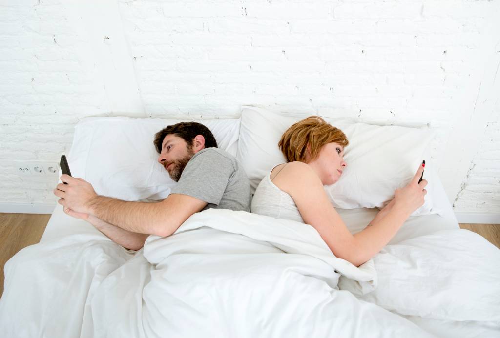couple using mobile phone in bed ignoring each other