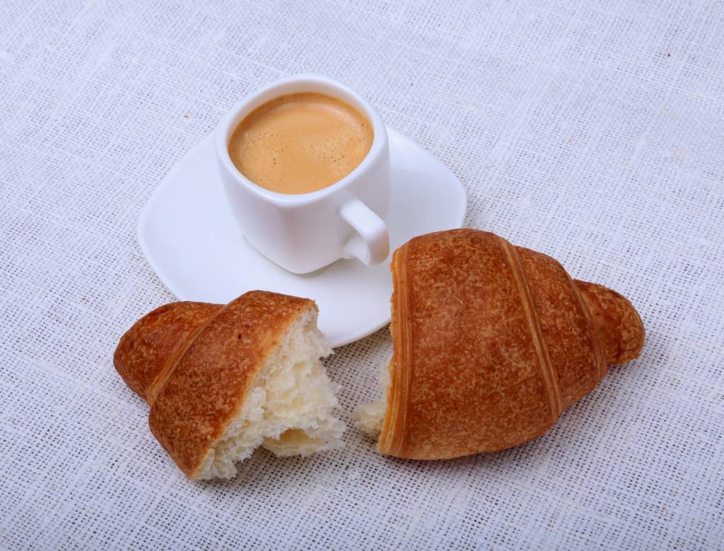 Crispy fresh croissants and cup of coffee espresso on a white background, morning breakfast, selective focus