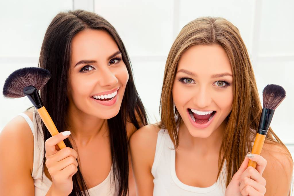 Erros que prejudicam a pele Compartilhar pinceis e cremes Portrait of happy beautiful women holding powder brushes
