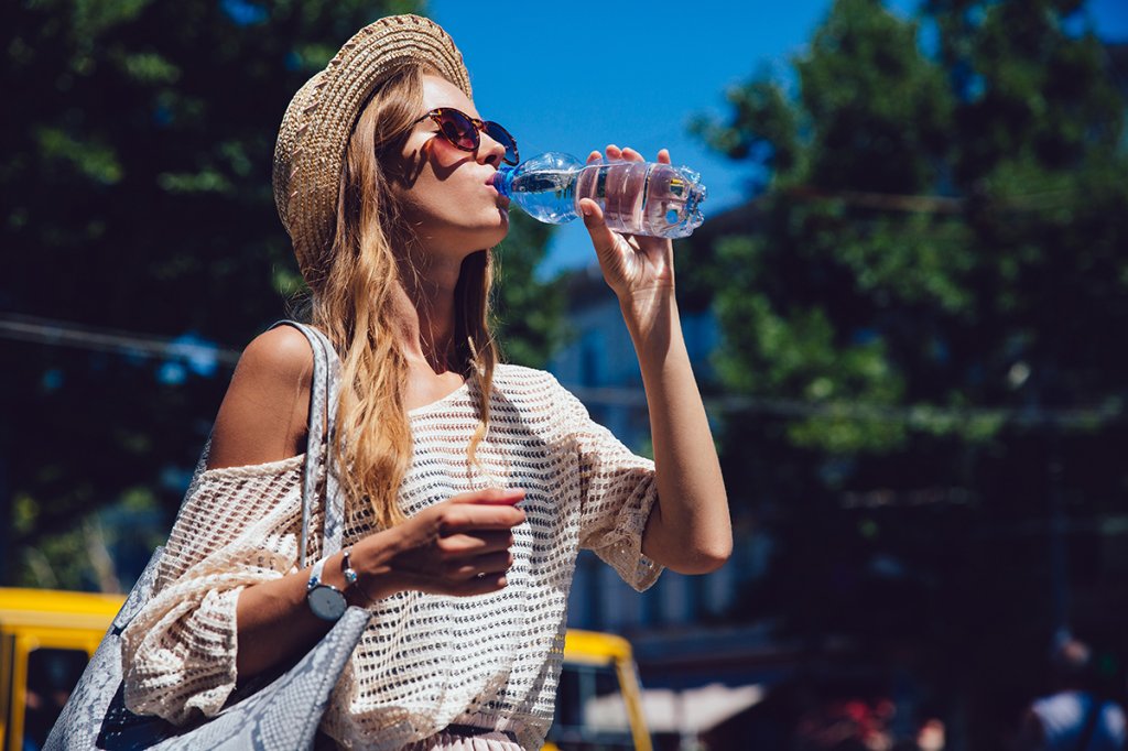 Trendy woman drinking a water from bottle, outdoors.