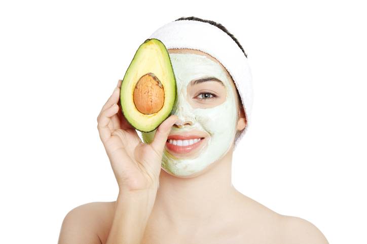 Pretty woman holding an avocado over her clay facial mask