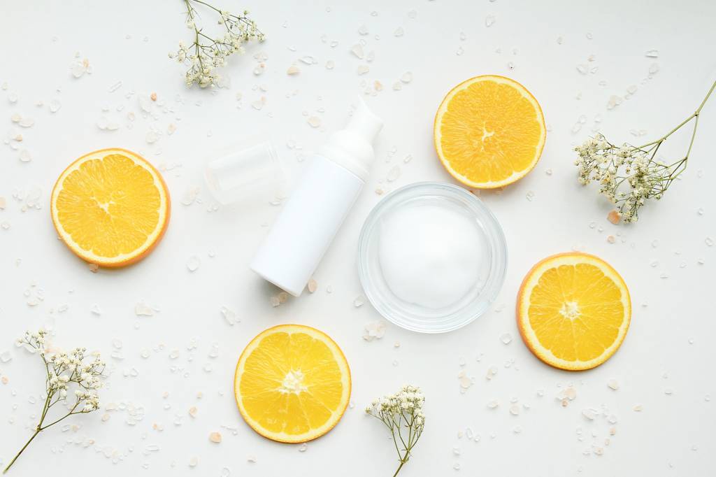 Vitamina C: contamos como e por que o nutriente pode salvar a sua pele Cosmetic foam pump bottle containers with fresh orange slices, Blank label for branding mock-up, Natural beauty product concept.