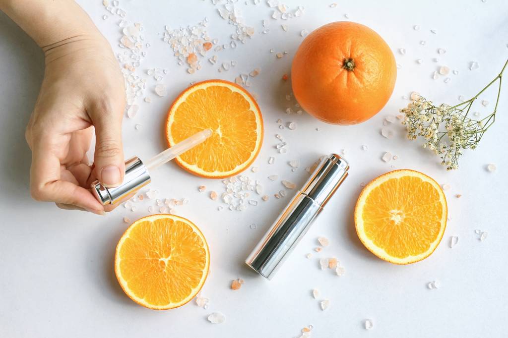 Vitamina C: contamos como e por que o nutriente pode salvar a sua pele Cosmetic bottle containers with fresh orange slices, Blank label for branding mock-up, Natural Vitamin C beauty product concept