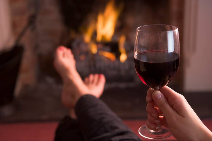 Feet warming at fireplace with hand holding wine