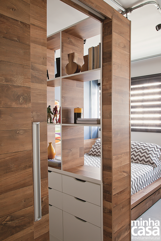 <span>É no quarto que o móvel curinga – queridinho dos arquitetos e do morador – mostra-se por completo. Dotado de uma porta deslizante, ele é composto de dois guarda-roupas (o fundo de um deles é o painel da TV que se vê na página anterior) e uma estante vazada. “Criamos uma grande caixa de madeira que dá privacidade ao dormitório sem isolar os espaços. E já que esse bloco não vai até o teto, permite que a luz natural alcance discretamente a sala, que não tem janela”, explicam os arquitetos </span><span>Erika Mello</span><span> e </span><span>Renato Andrade</span><span>. O morador </span><span>Felipe Brandão</span><span>, por sua vez, ressalta o que mais gostou: “Tudo o que eu precisava guardar coube neste closet!”. </span> <span>É no quarto que o móvel curinga – queridinho dos arquitetos e do morador – mostra-se por completo. Dotado de uma porta deslizante, ele é composto de dois guarda-roupas (o fundo de um deles é o painel da TV que se vê na página anterior) e uma estante vazada. “Criamos uma grande caixa de madeira que dá privacidade ao dormitório sem isolar os espaços. E já que esse bloco não vai até o teto, permite que a luz natural alcance discretamente a sala, que não tem janela”, explicam os arquitetos </span><span>Erika Mello</span><span> e </span><span>Renato Andrade</span><span>. O morador </span><span>Felipe Brandão</span><span>, por sua vez, ressalta o que mais gostou: “Tudo o que eu precisava guardar coube neste closet!”. </span>