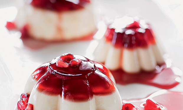 receita-panna-cotta-morango-roma Há três doces circulares, com as bordas desenhadas. Com textura de gelatina, eles têm uma base de creme branco e o topo vermelho, cobertos com sementes de roma.