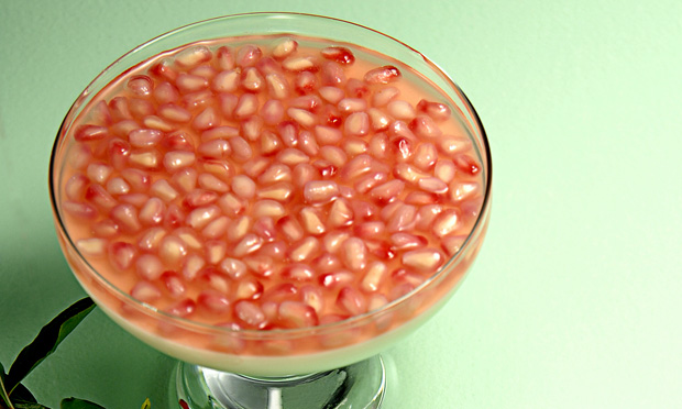 receita-parfait-de-roma Em uma taça de vidro aparecem muitas sementes de romã envolvidas por um líquido avermelhado e translúcido. A taça está sobre uma superfície verde