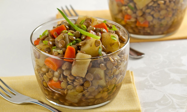 receita-salada-de-lentilha-com-legumes Em um copo de vidro está a salada de lentilha com pedaços de azeitona, vagem e cenoura. Ao fundo, desfocado, aparece outro copo e um garfo.