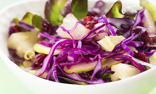 receita-salada-repolho-roxo-roma Em uma tigela branca está uma salada com repolho fatiado fino, pedaços de palmito e sementes de romã