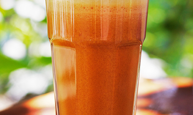 receita-suco-desintoxicante-boa-forma Um copo de suco de cor laranja cheio aparece sobre um fundo desfocado verde
