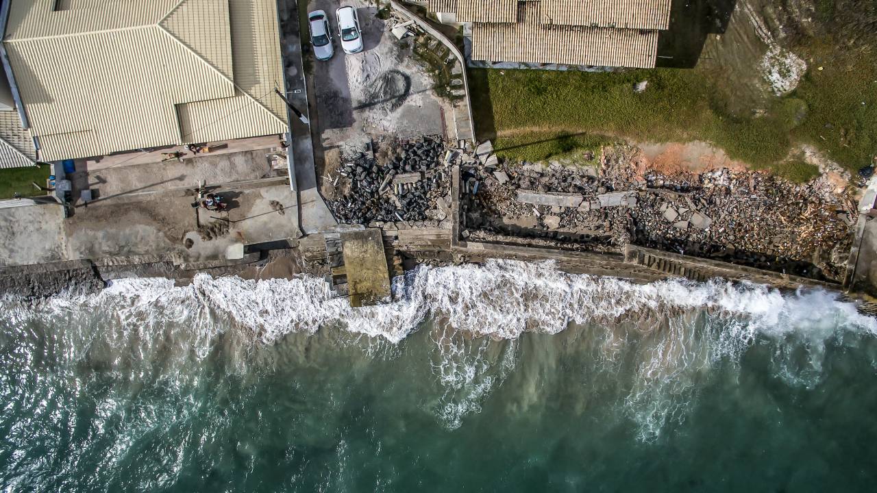 Imagem aérea. O mar invade a faixa de construção bem próxima à faixa de areia