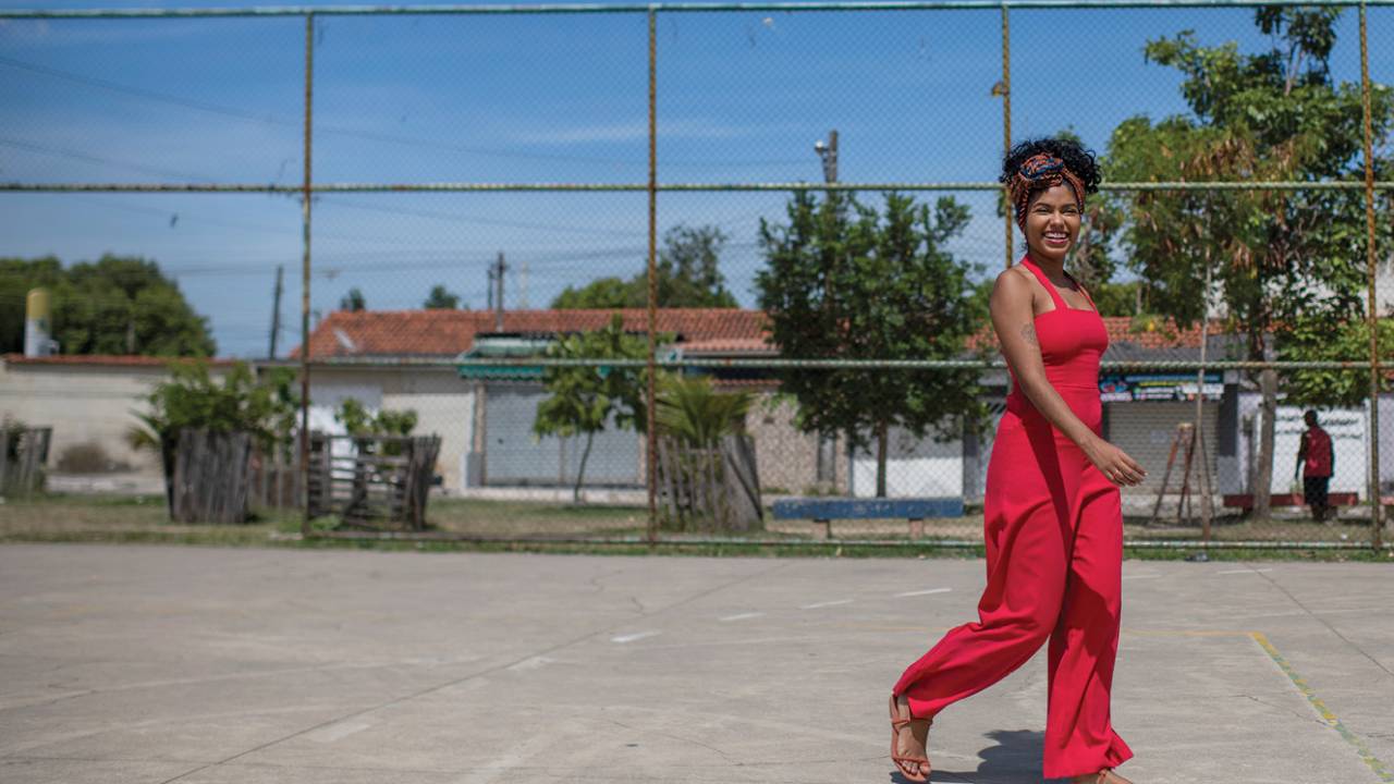 Joyce usa macacão vermelho e caminha por quadra de esportes