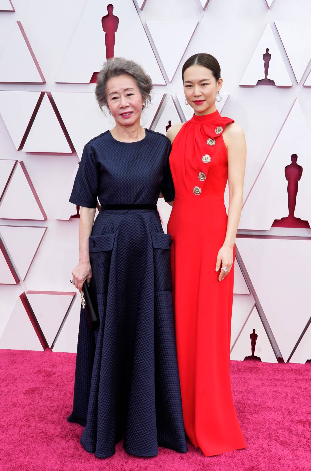 93rd Annual Academy Awards – Arrivals As atrizes são orientais. Do lado esquerdo, Youn tem cabelos grisalhos presos. Ela usa um vestido com mangas curtas tipo camiseta, azul marinho. Já Han usa um vestido vermelho com gola alta, sem mangas e detalhes dourados