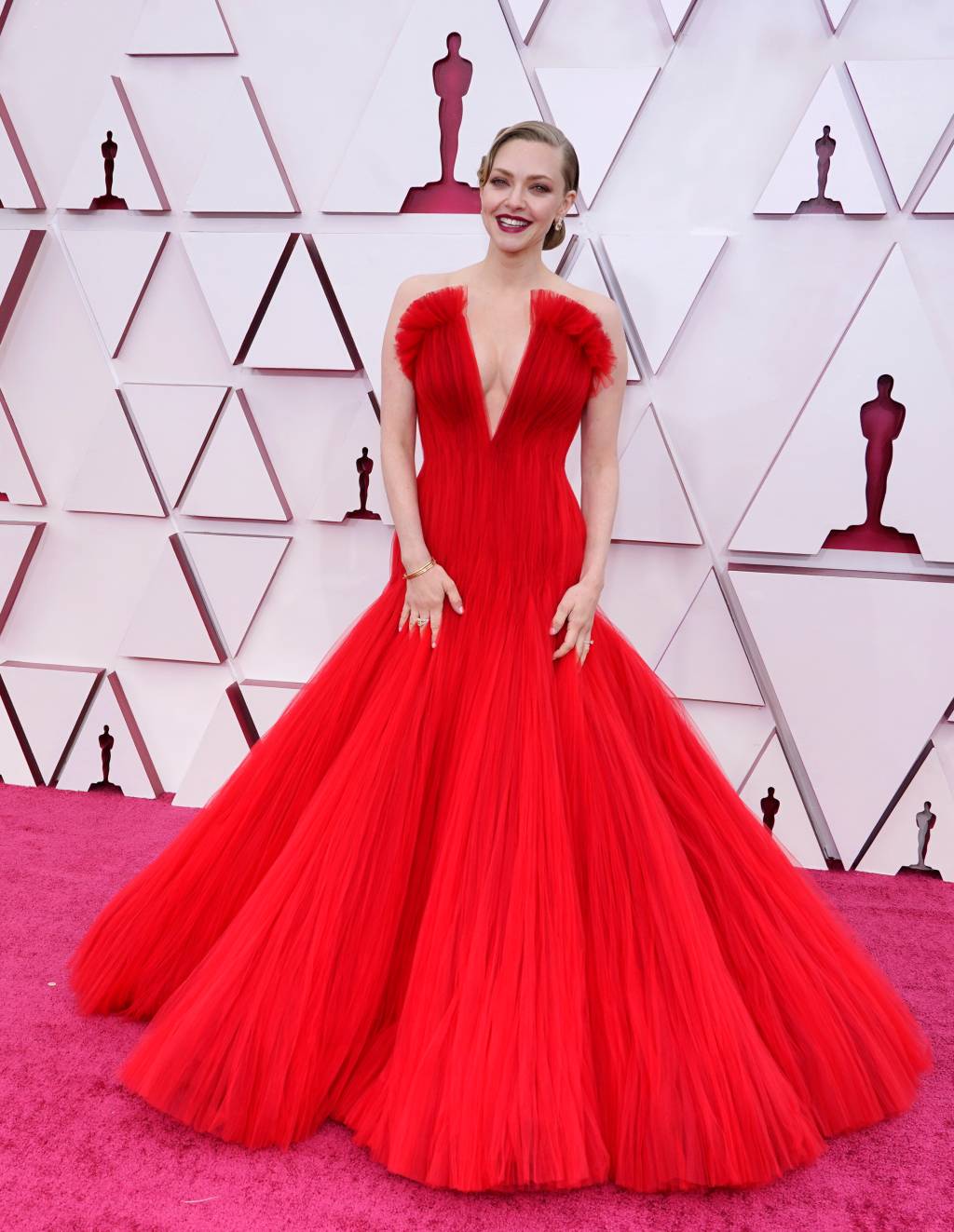 93rd Annual Academy Awards – Arrivals Amanda é uma mulher branca, loira. Ela usa um vestido vermelho com volume no decote, que desce em V até a barriga e saia volumosa