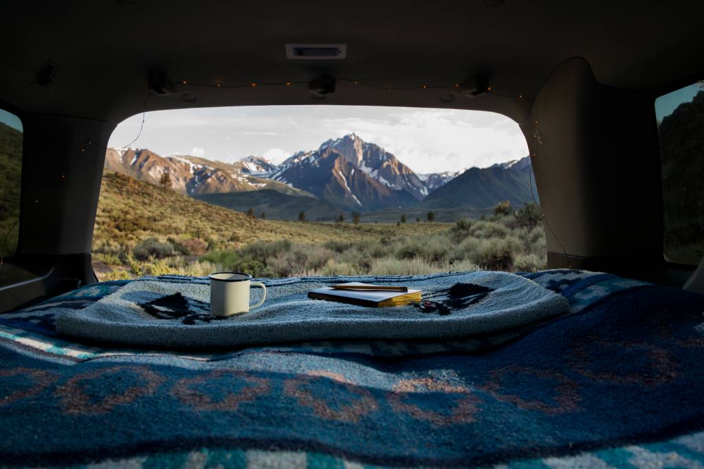 Book and mug on blanket at car trunk with Mount Morrison in background acampamento