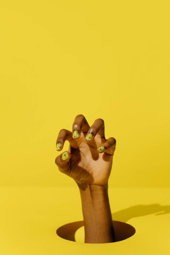 roer-unhas-parar-crescimento-fortalecimento Mão com unhas decoradas no fundo amarelo