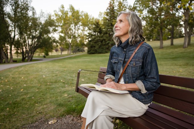 Happy senior woman reading book on park bench