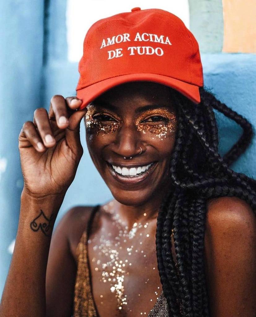 O-que-é-Glitter-5-formas-de-utilizar-o-glitter-no-Carnaval-maquiagem-cabelo-Carnaval-2024 Mulher utilizando um boné vermelho e com o rosto e corpo coberto por glitters