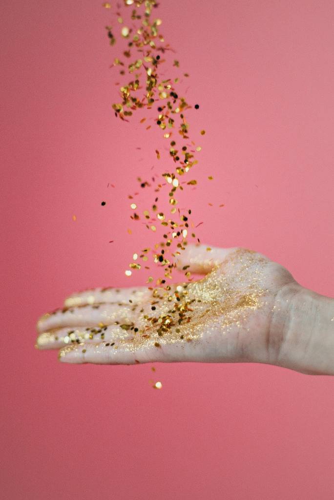glitter-comum-faz-mal-5-opções-sustentáveis-para-fazer-a-substituição Glitters dourados caindo sobre a mão de uma modelo