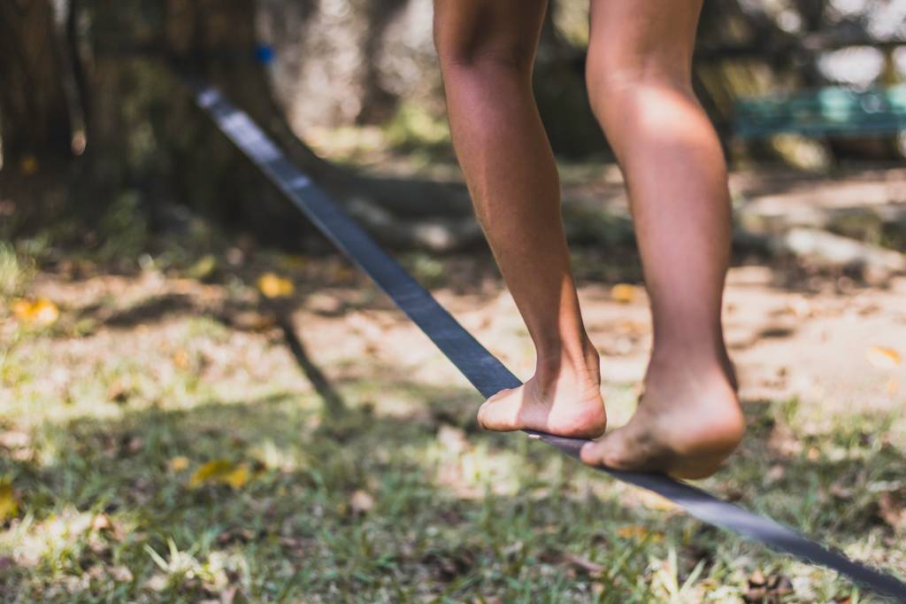 Corda bamba Pés andando na corda bamba ou no slackline ao ar livre em um parque da cidade com luz de fundo. Indicação de emoções como medo e frio na barriga