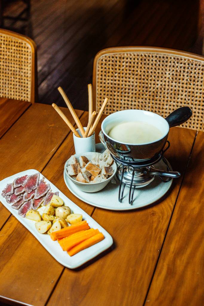 O restaurante, que fica dentro da fábrica da Dengo, é uma ótima opção para o fim de semana – já que, além da refeição, também é possível conhecer o processo de produção das barras bean-to-bar. Para começar, o local traz duas opções principais: o Fondue de Queijo Tradicional (R$ 129,90) e o Fondue de Queijo Vegano (R$ 129,90), ambos acompanhados de pães de fermentação natural, batata bolinha, grissini, cenoura e cogumelos portobello. Para uma experiência ainda mais especial, é possível adicionar acompanhamentos como carne de sol (R$ 149,90) ou frutos do mar (R$ 159,90).