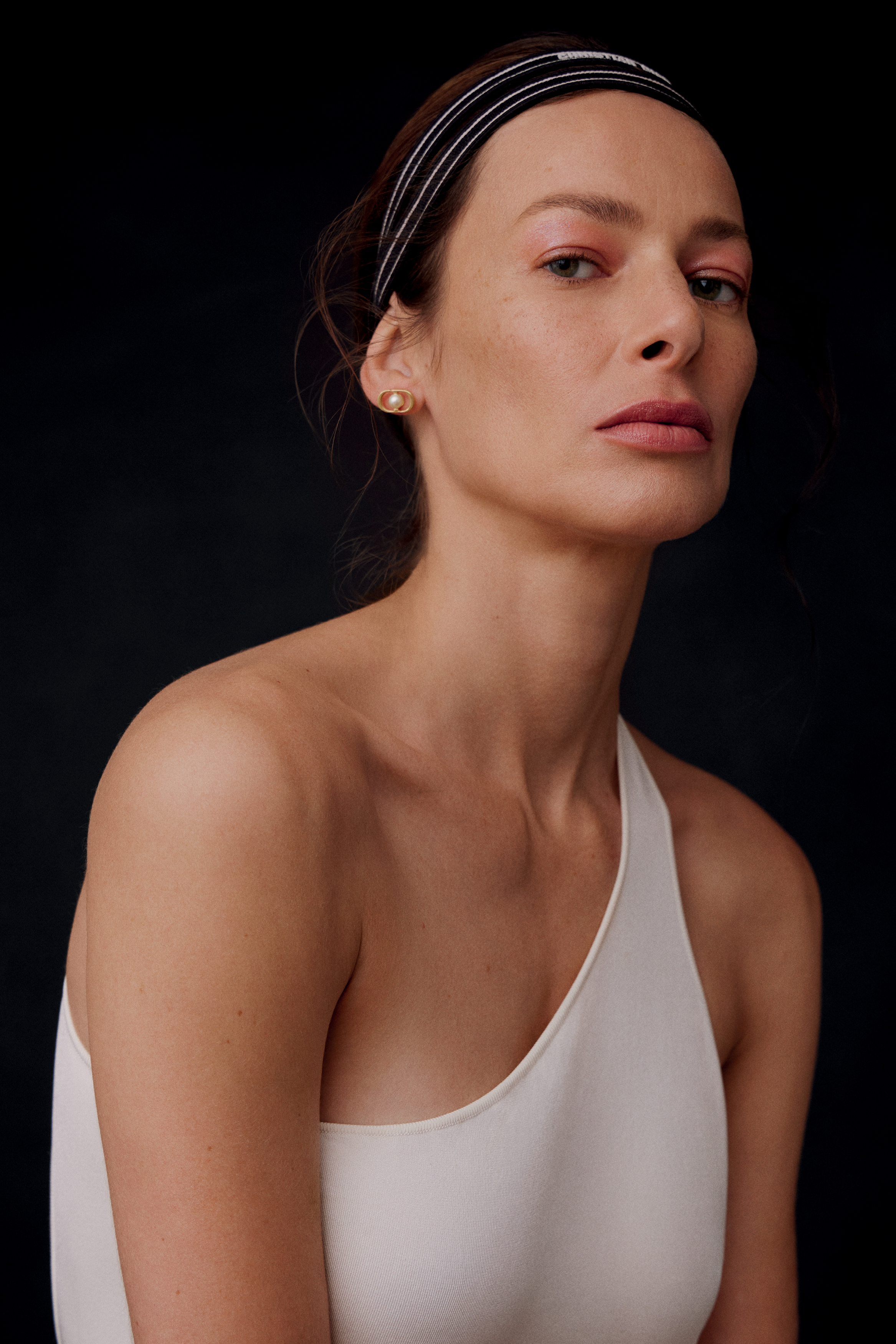 Imagem de mulher branca exibindo maquiagem delicada e feminina. O fundo &eacute; preto e ela usa uma regata de manga &uacute;nica.