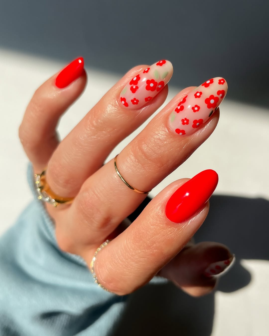 Imagem mostra unhas vermelhas com nail art de flores.