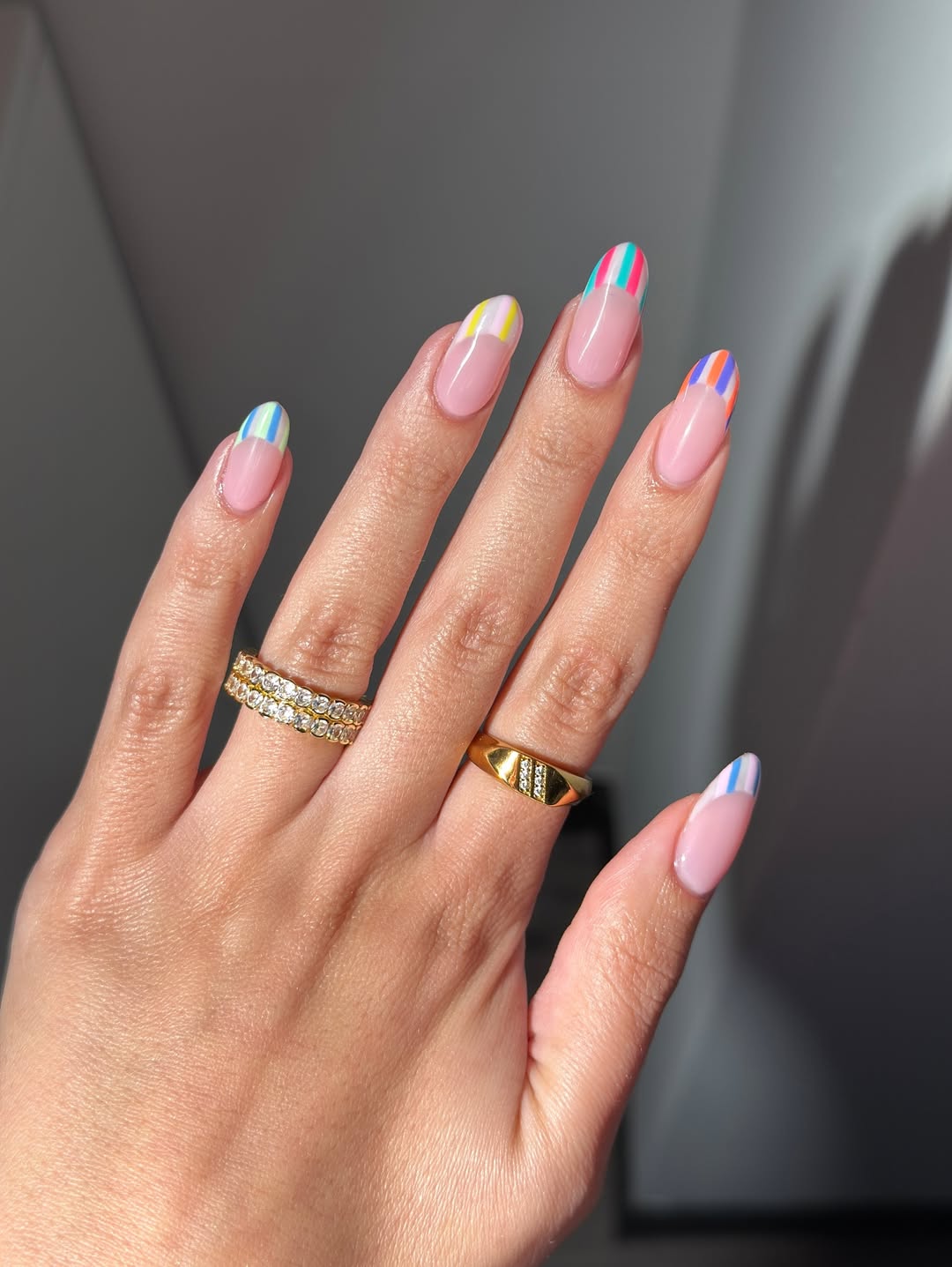 Foto de uma m&atilde;o com as unhas amendoadas. As unhas est&atilde;o com a nail art de uma francesinha em listras coloridas