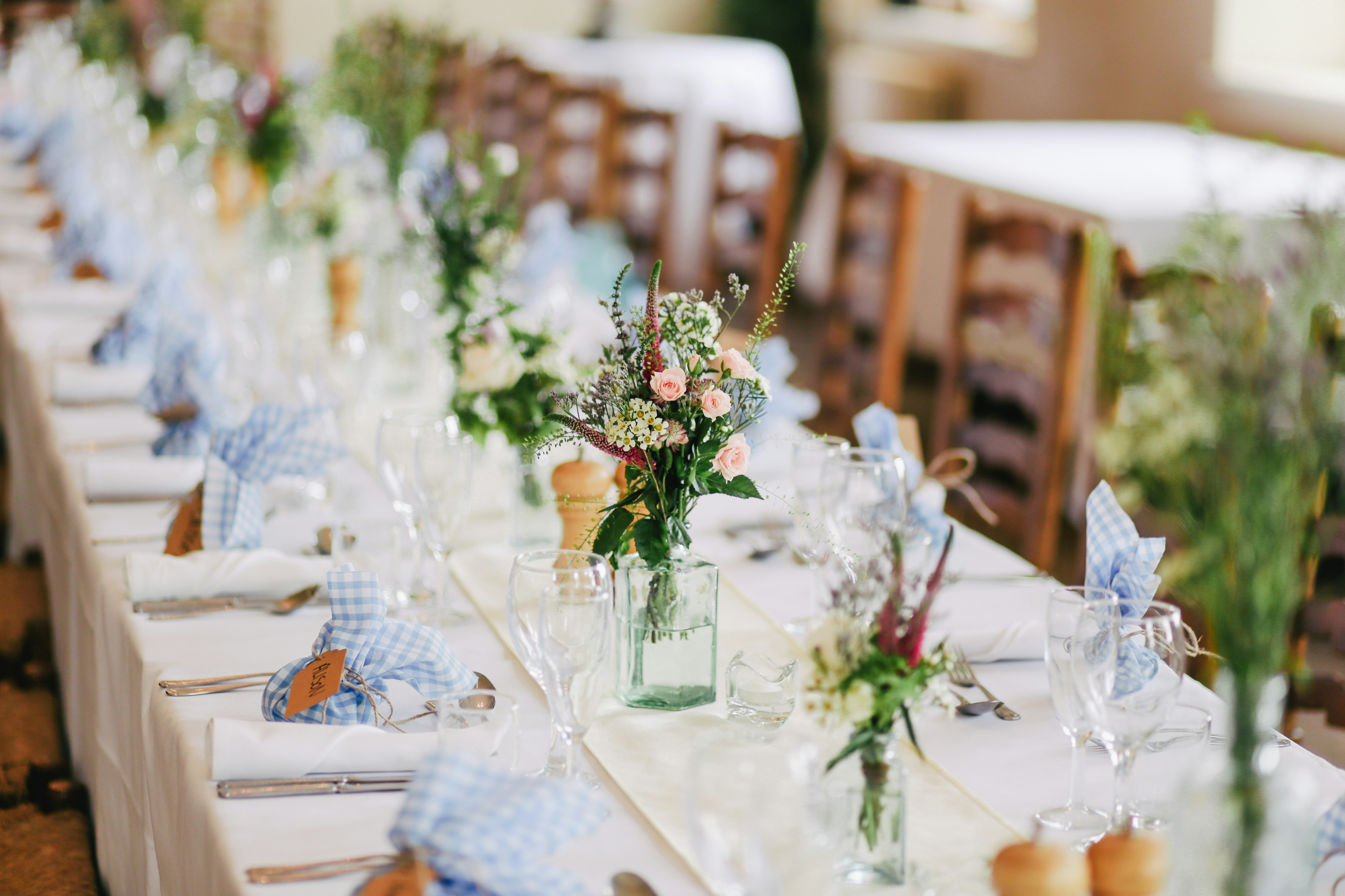 Mesa retangular de casamento com toalha bege e flores em vasos de vidro