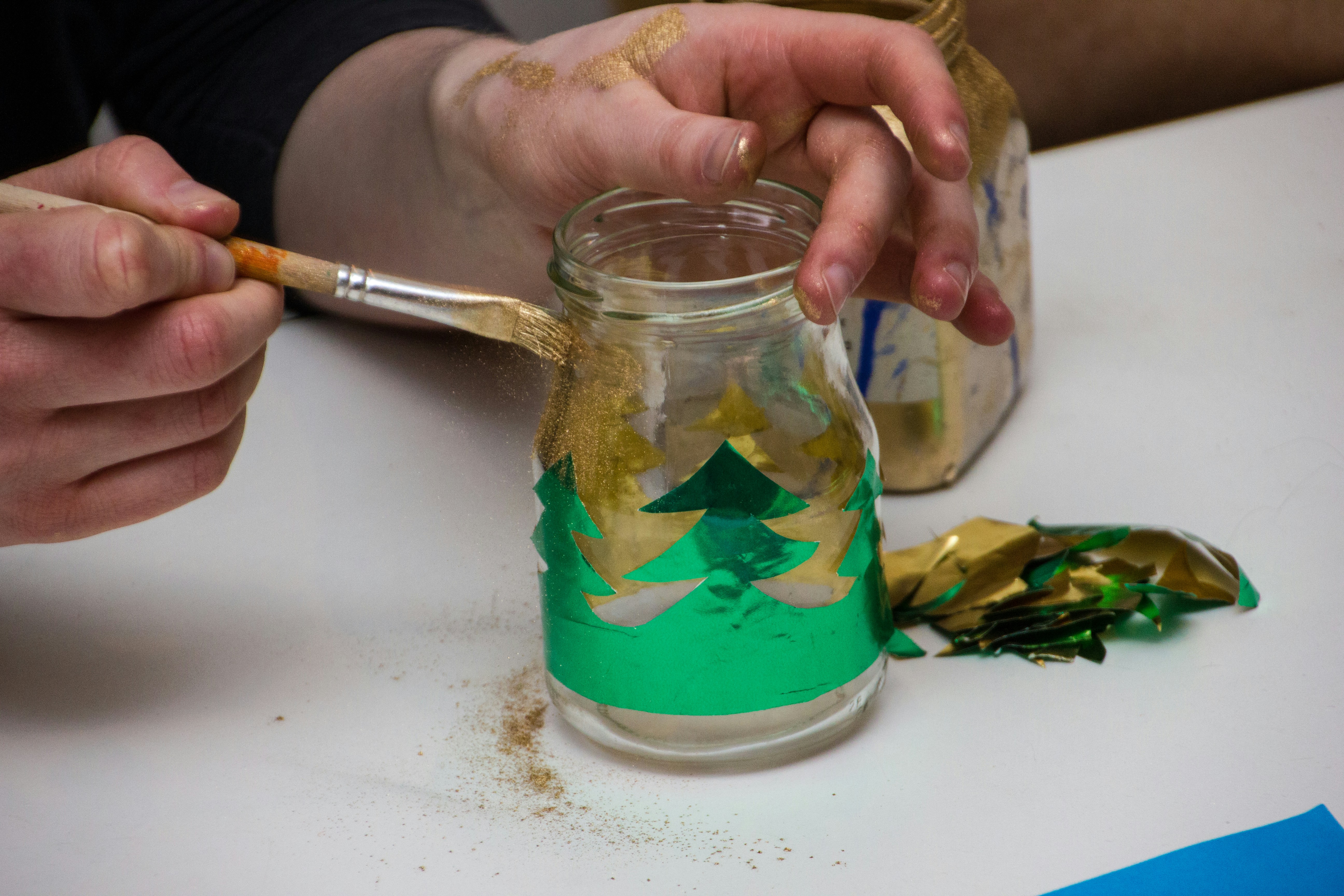 Pessoa pintando pote de vidro com tintas verde e dourada