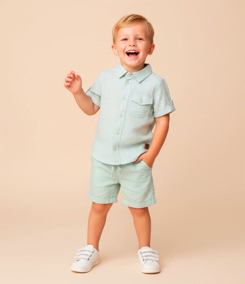 Foto de um menino loiro usando um conjuntinho masculino composto por camisa social verde com mangas curtas e bermuda de sarja verde